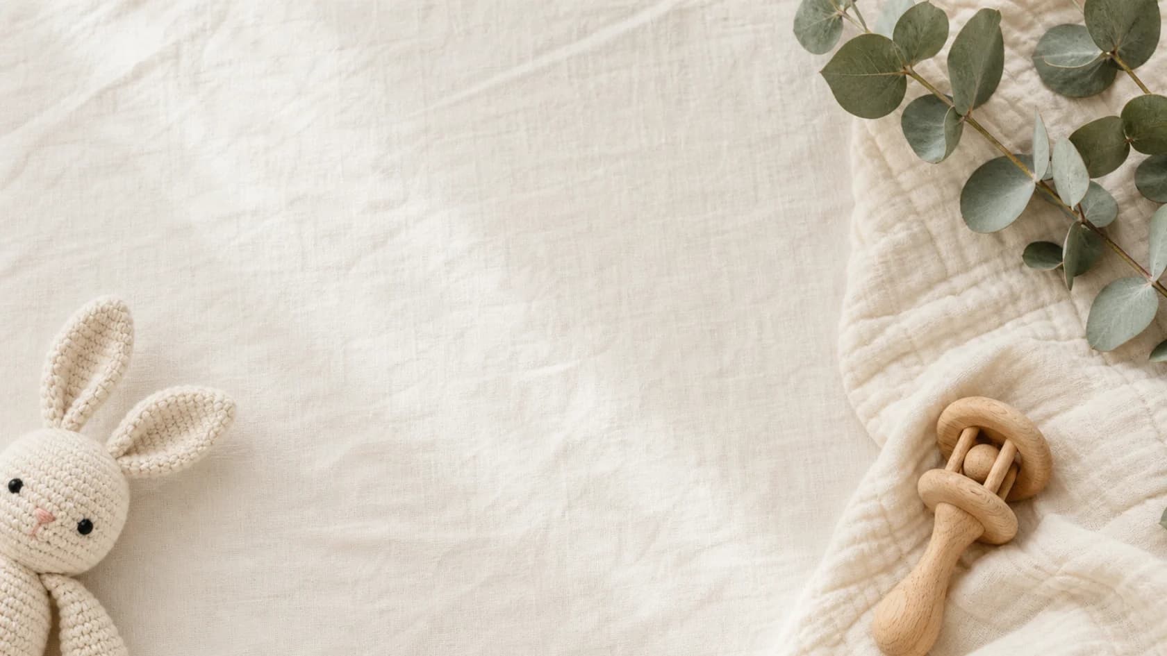 A calm nursery scene with a knitted rabbit, wooden rattle and folded baby blanket